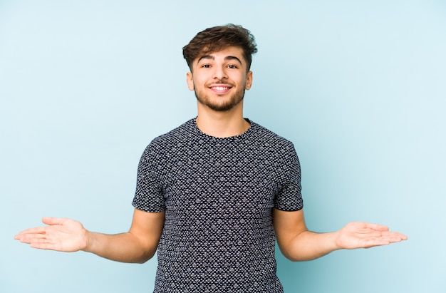 Jeune homme arabe sur un mur bleu montrant une expression bienvenue.