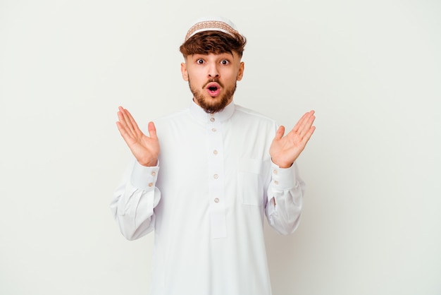 Jeune homme arabe portant le costume arabe typique isolé sur fond blanc surpris et choqué.