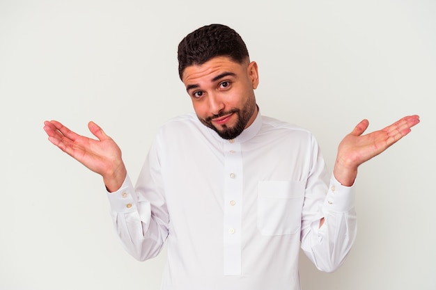 Jeune homme arabe portant des vêtements arabes typiques isolés sur fond blanc doutant et haussant les épaules dans le geste d'interrogation.