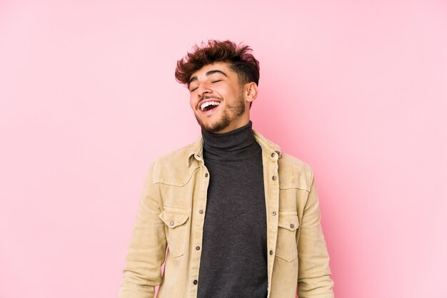 Jeune homme arabe posant dans un mur détendu et heureux de rire, le cou tendu montrant les dents.