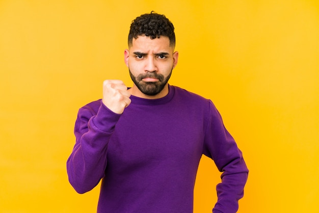 Jeune homme arabe de race mixte isolé montrant le poing à la caméra, une expression faciale agressive.