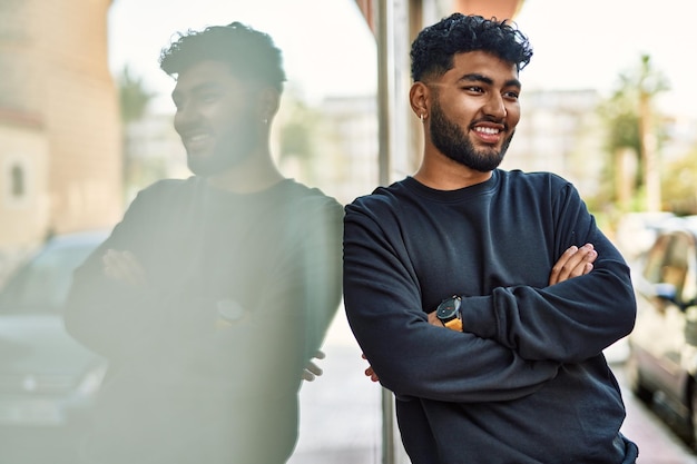 Jeune homme arabe souriant confiant appuyé sur le mur de la rue