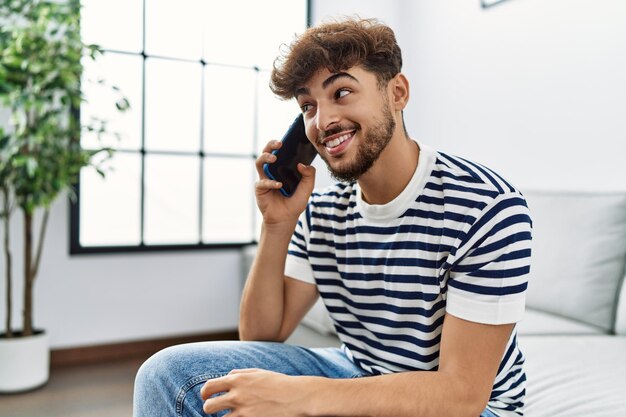 Photo jeune homme arabe souriant confiant parlant sur le smartphone à la maison