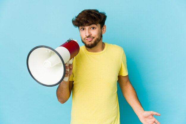 Jeune homme arabe tenant un mégaphone confus, se sent douteux et incertain.