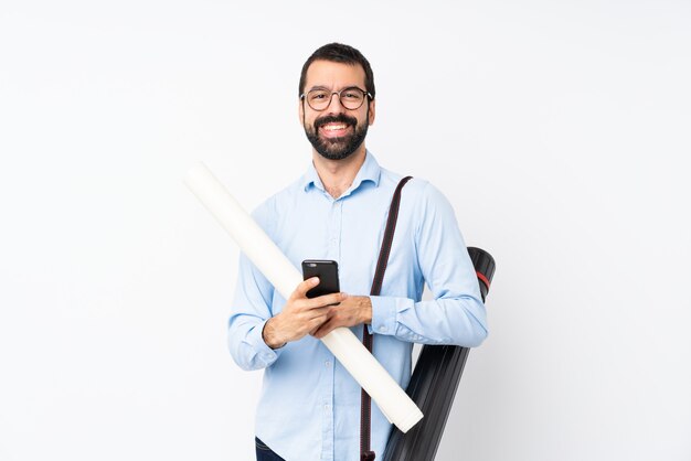 Jeune homme architecte avec barbe sur blanc isolé en envoyant un message avec le mobile