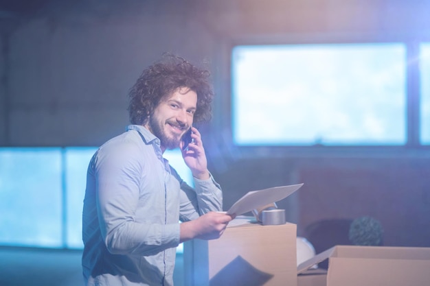 jeune homme architecte sur le chantier de construction vérifiant les documents et le flux de travail d'entreprise à l'aide d'un téléphone portable avec des boîtes en carton autour de lui dans un nouveau bureau de démarrage