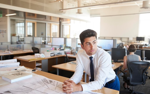 Jeune homme architecte s'appuyant sur un bureau dans un bureau à aire ouverte