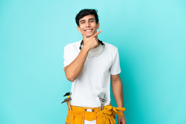 Jeune homme argentin électricien isolé sur fond bleu heureux et souriant