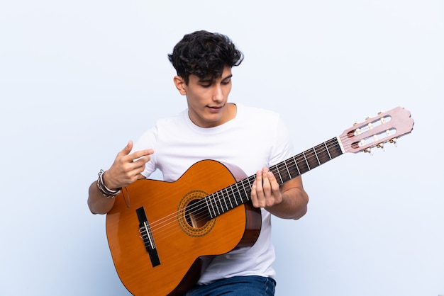 Jeune homme argentin avec guitare sur mur bleu isolé