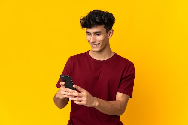 Jeune homme argentin isolé sur fond jaune l'envoi d'un message ou d'un e-mail avec le mobile