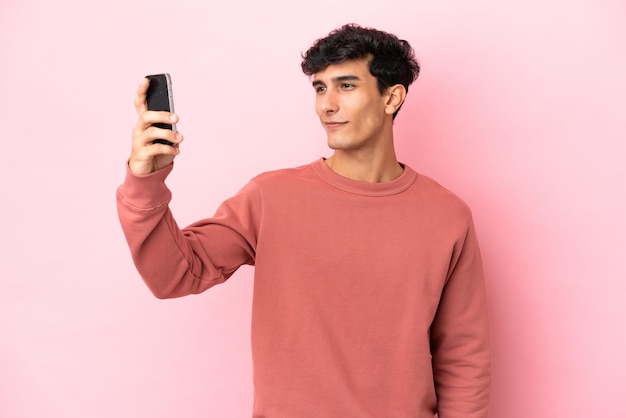 Jeune homme argentin isolé sur fond rose faisant un selfie