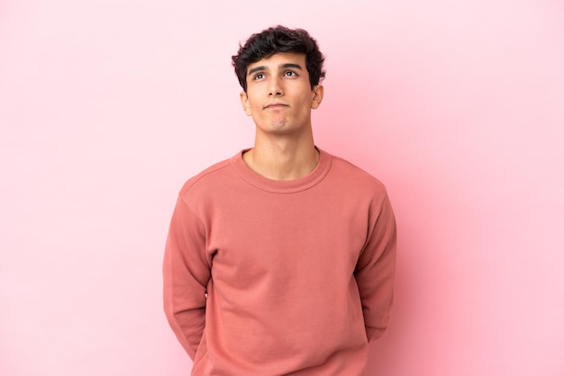Jeune homme argentin isolé sur fond rose et levant les yeux