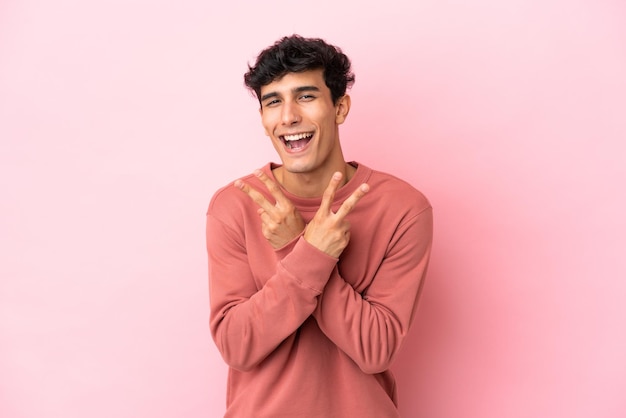 Jeune homme argentin isolé sur fond rose souriant et montrant le signe de la victoire