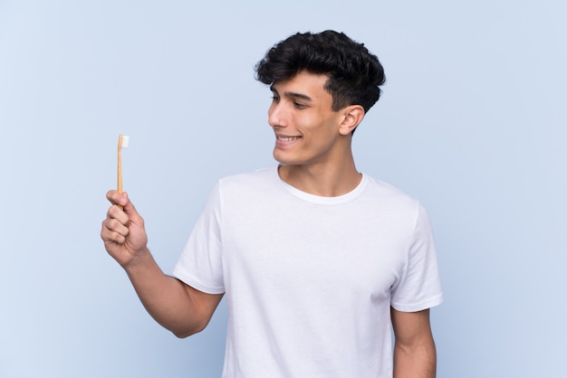 Jeune homme argentin se brosser les dents sur le mur bleu isolé avec une expression heureuse