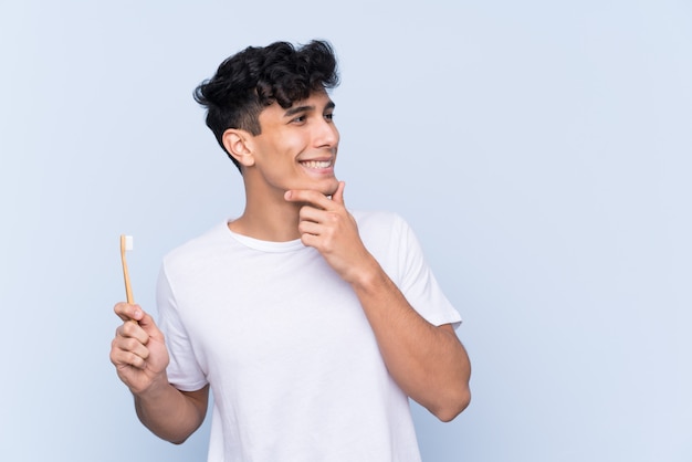 Jeune homme argentin se brosser les dents sur le mur bleu isolé en pensant à une idée et à côté