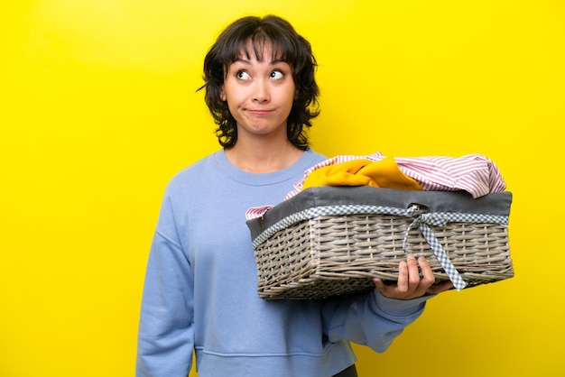 Jeune homme argentin tenant un panier à linge isolé sur fond jaune et levant les yeux