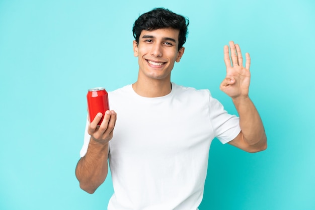 Jeune homme argentin tenant un rafraîchissement isolé sur fond bleu heureux et comptant quatre avec les doigts