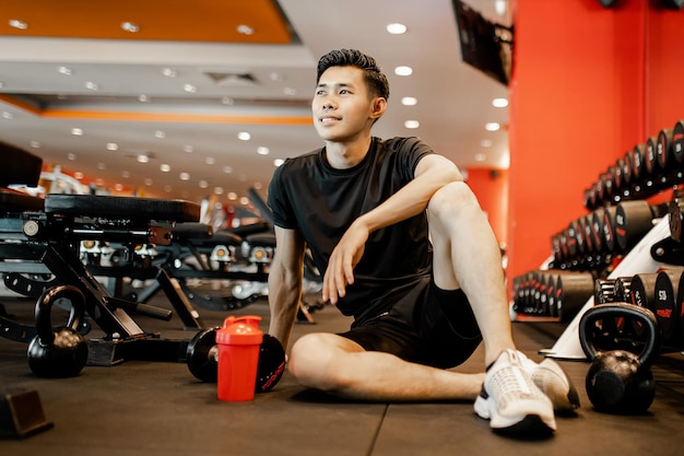 Jeune homme asiatique assis se reposer après l'entraînement pour une bonne santé dans la forme physique Concept d'exercice de style de vie et de sport