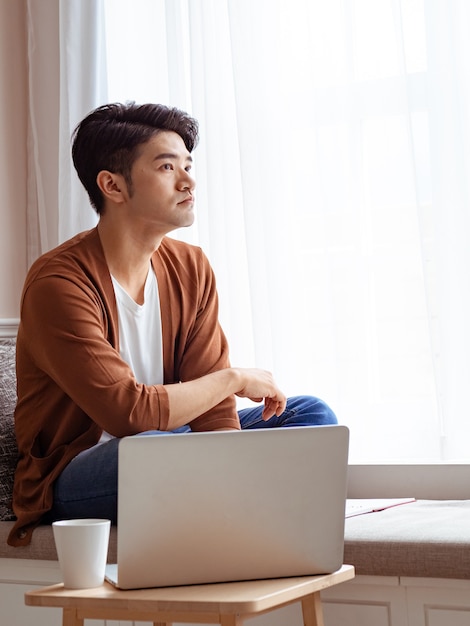 Jeune homme asiatique assis à la table devant un ordinateur portable