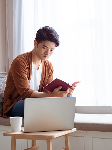 Jeune homme asiatique assis à la table devant un ordinateur portable