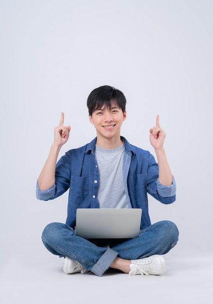 Jeune homme asiatique assis et utilisant un ordinateur portable sur fond blanc