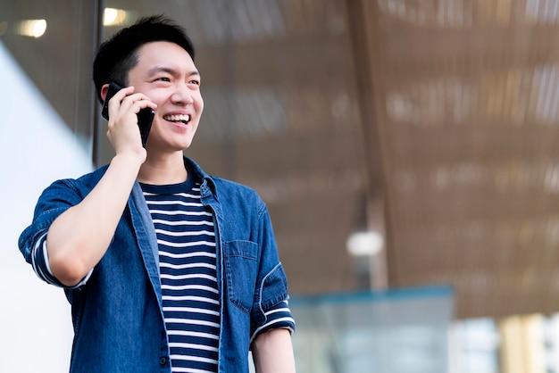 Jeune homme asiatique attrayant et confiant portant un tissu casul main tenir un smartphone connecter la communication près d'un bâtiment moderne concept d'idées de technologie intelligente