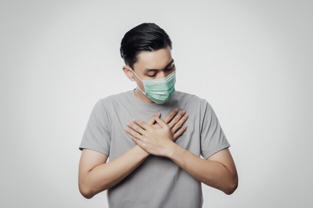 Jeune homme asiatique au masque hygiénique souffrant de maux de gorge, 2019-nCoV ou coronavirus. Maladies respiratoires aéroportées telles que les combats pm 2.5 et la grippe. Projectile studio, isolé, blanc