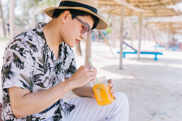 Jeune homme asiatique, boire du jus d'orange sur la plage