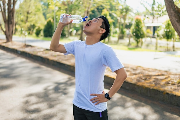 Jeune homme asiatique buvant de l'eau après une séance d'entraînement dans le parc