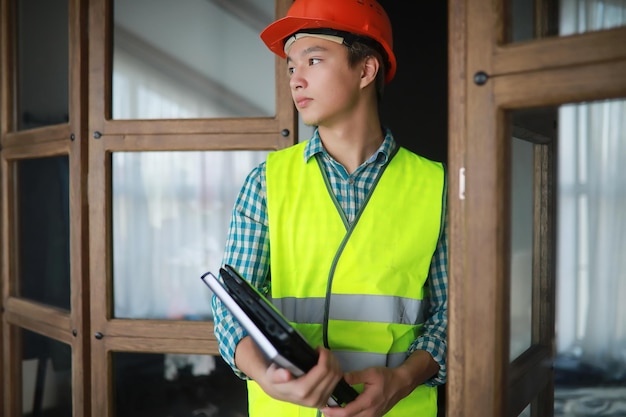 Jeune homme asiatique en casque de protection et gilet de construction