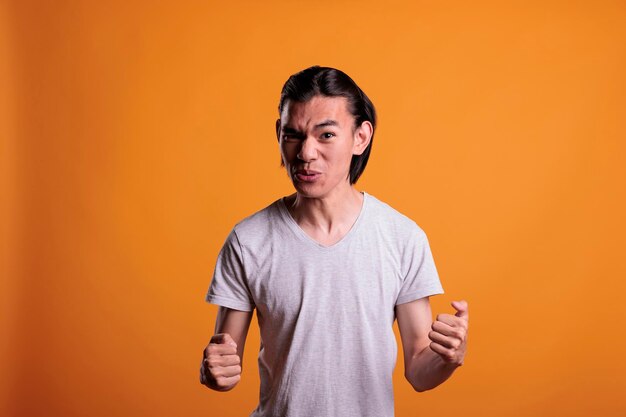 Jeune homme asiatique en colère serrant les poings avec un portrait d'expression faciale furieux. Personne irritée criant, regardant la caméra, montrant une émotion de rage, vue de face plan moyen