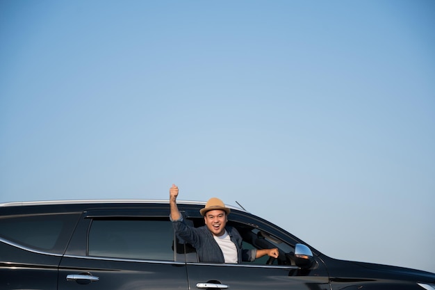 Un jeune homme asiatique conduit une voiture par temps clair. Avec un beau ciel bleu. Il conduit pour voyager en voiture.