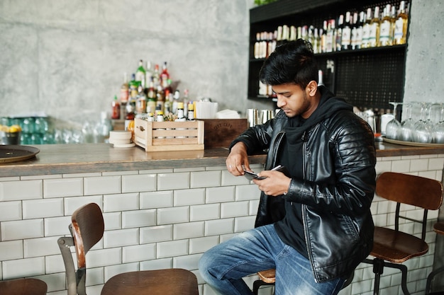 Jeune homme asiatique décontracté et élégant portant une veste en cuir assis sur un bar et regardant son portefeuille