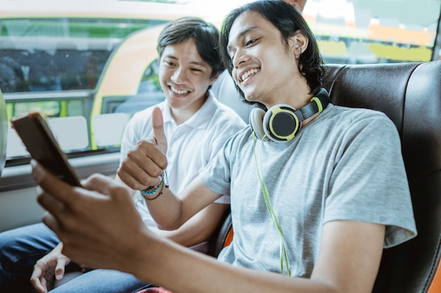 Un Jeune Homme Asiatique Avec Des écouteurs Et Utilisant Un Téléphone Portable Pour Des Appels Vidéo Avec Un Coup De Pouce Alors Qu'il était Assis Près D'une Fenêtre Dans Un Bus