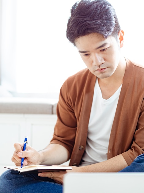 Jeune homme asiatique écrit dans un cahier.