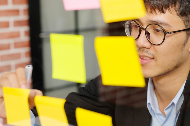 Jeune homme asiatique écrit sur pense-bête au bureau, business, idées de création de brainstorming, style de vie de bureau, succès dans le concept d'entreprise