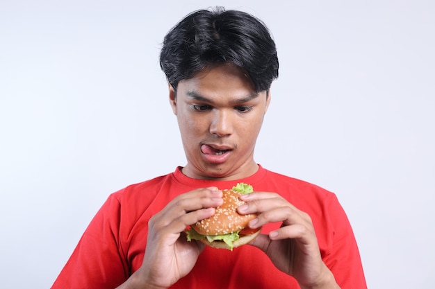 Un jeune homme asiatique enchanté regardant un délicieux hamburger isolé sur un fond blanc