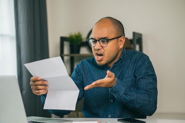 Un jeune homme asiatique est stressé parce qu'il regarde de nombreuses notes de frais et qu'il n'a pas d'argent à payer