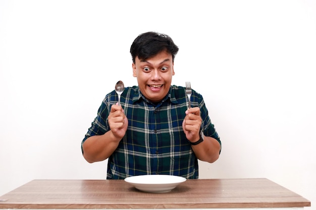 Un jeune homme asiatique excité montrant le pouce en l'air avec un plat vide sur la table.