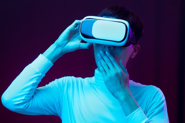 Jeune homme asiatique excité portant un casque VR à la lumière du néon, concept de technologie future.