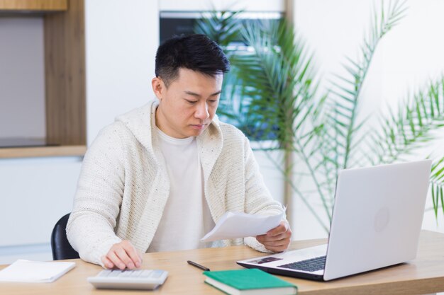 jeune homme asiatique faisant de la paperasse à la maison assis à un bureau