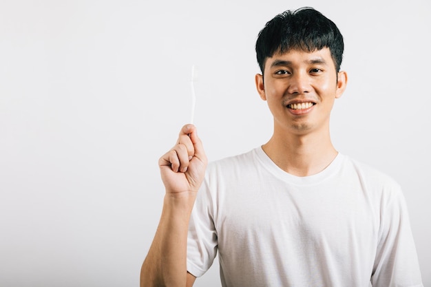 Un jeune homme asiatique favorise la santé dentaire en se brossant les dents en toute confiance. Prise de vue en studio isolée sur fond blanc, montrant l'importance des soins bucco-dentaires.