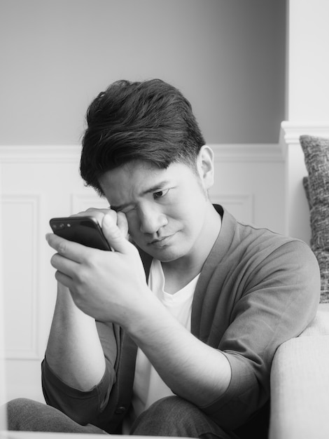 Jeune homme asiatique frottant ses yeux fatigués son smartphone