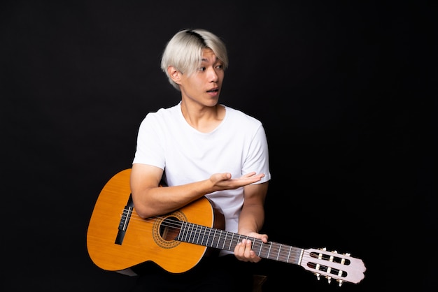 Jeune homme asiatique avec guitare sur noir avec une expression faciale surprise