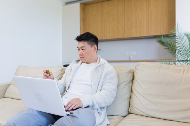 jeune homme asiatique heureux faisant du shopping en ligne dans une boutique internet à l'aide d'un ordinateur portable et d'une carte de crédit