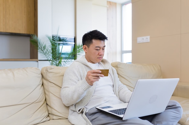 jeune homme asiatique heureux faisant du shopping en ligne dans une boutique internet à l'aide d'un ordinateur portable et d'une carte de crédit