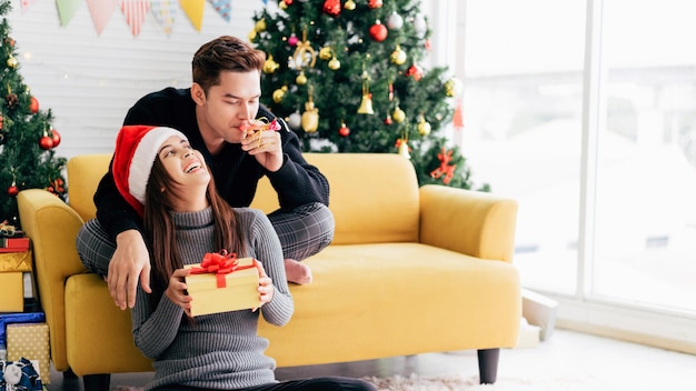 Un jeune homme asiatique heureux soufflant un sifflet de fête dans le dos de sa petite amie portant un Père Noël