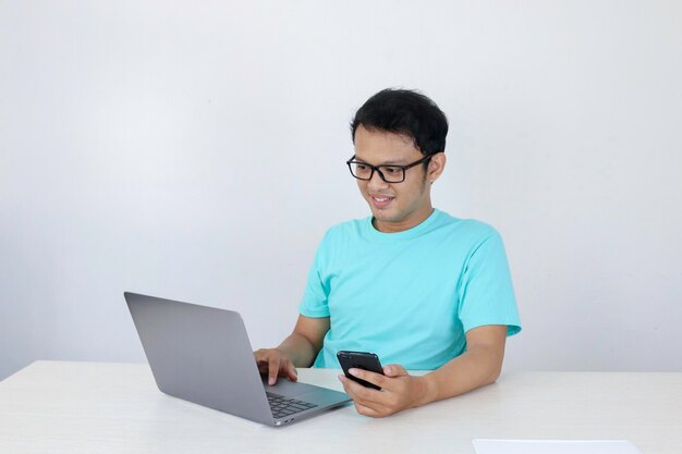 Jeune homme asiatique heureux et sourire quand il voit sur un téléphone intelligent avec un ordinateur portable à côté de lui un homme indonésien portant une chemise bleue