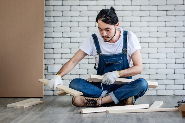 Jeune homme asiatique hipster travaillant comme bricoleur, assemblant une table en bois avec des équipements, concept de bricolage à domicile et libre-service à la maison.