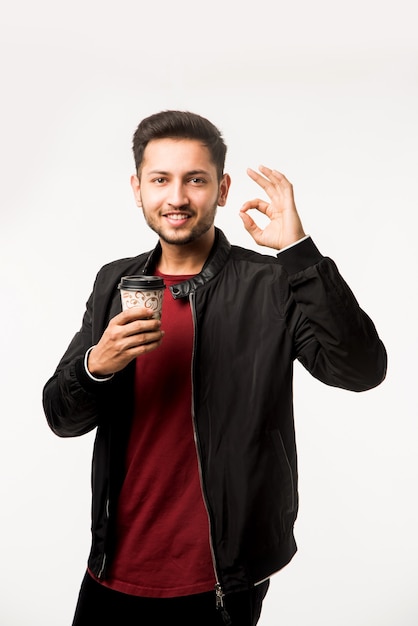 Jeune homme asiatique indien tenant une tasse de café en papier avec un capuchon en plastique noir isolé sur fond blanc dans le studio, café publicitaire